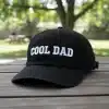 Black unstructured cotton dad hat with COOL DAD embroidery, curved brim and adjustable metal strap